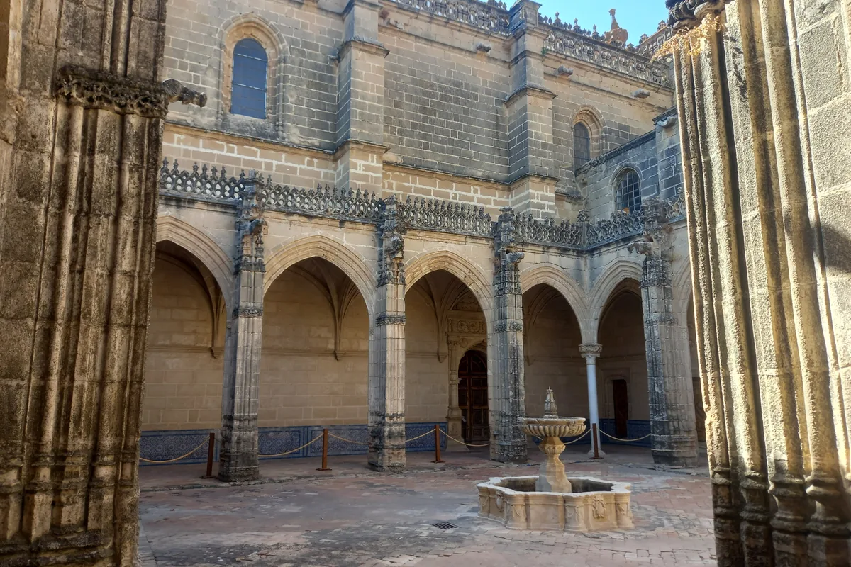 Un pequeño claustro gótico con arcos apuntados y una fuente de piedra en su patio, visto entre dos columnas talladas